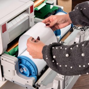 Woman adjusting a roll of new photo paper on a photographic printer in a printing house or studio in a close up view of her hands